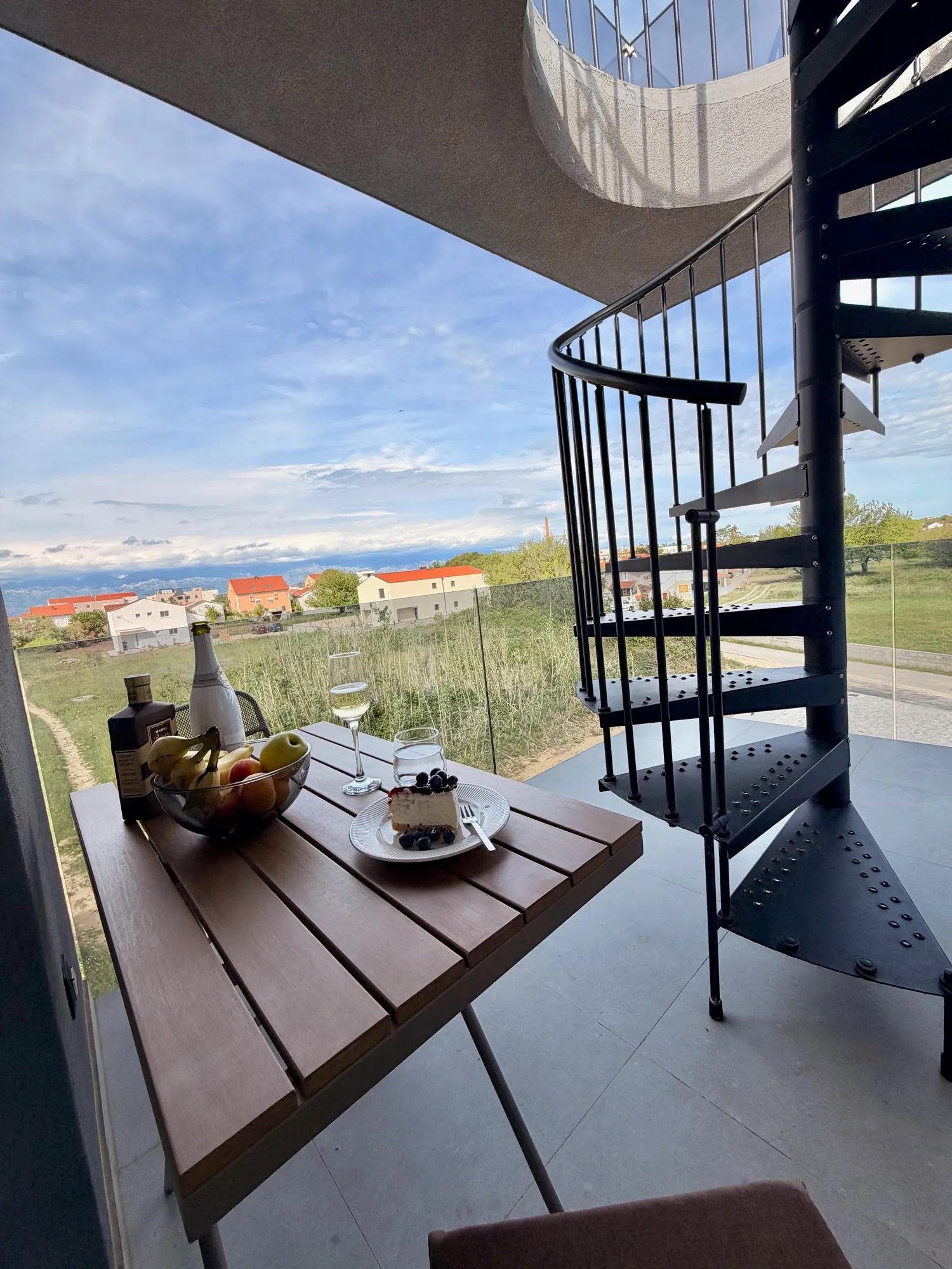 Balkon s postavljenim sklopivim stolom i spiralnim stepenicama na krovnu terasu, iza more