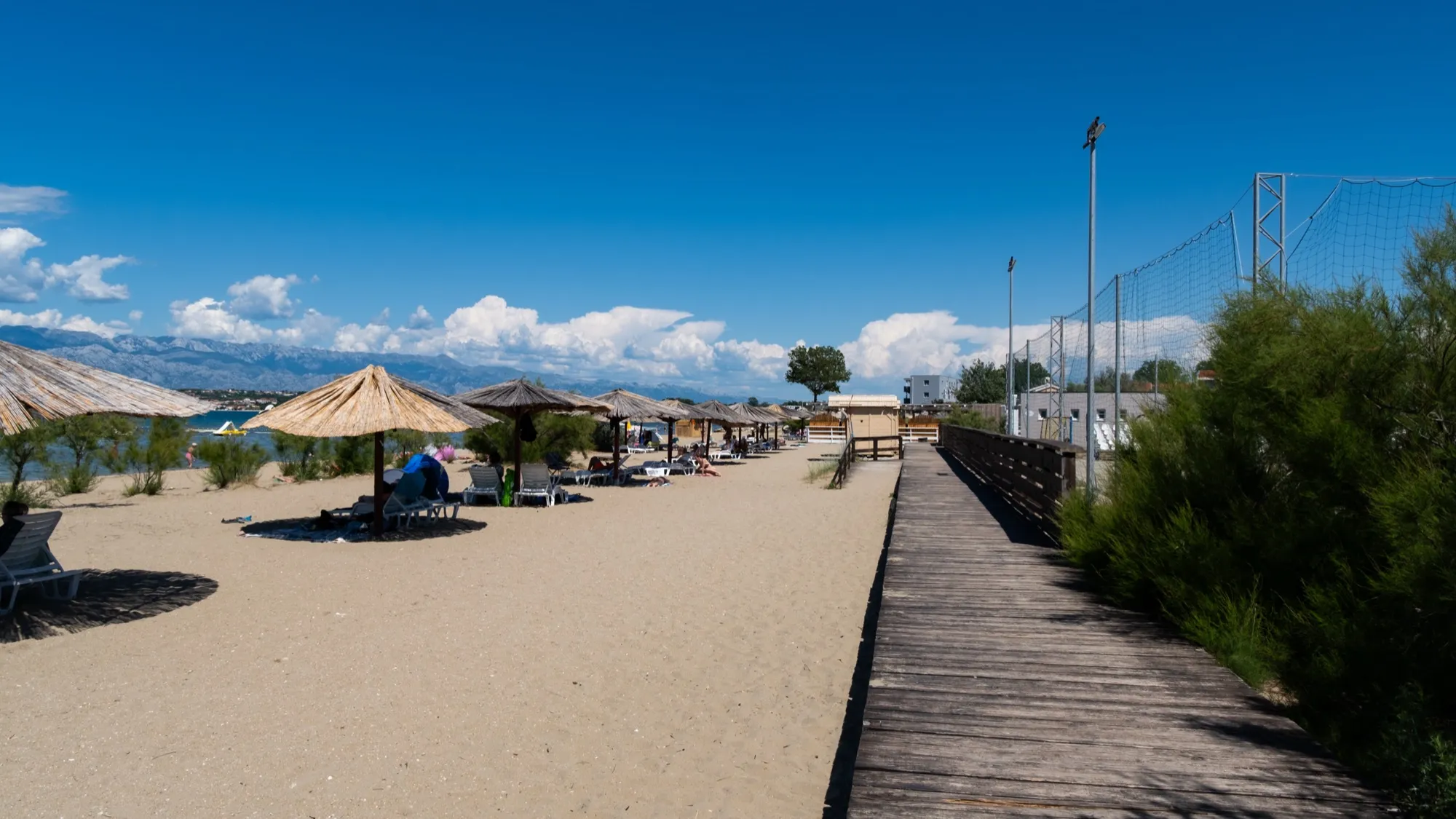 Plaža Ždrijac sa suncobranima i drvenom stazom, u pozadini Velebit