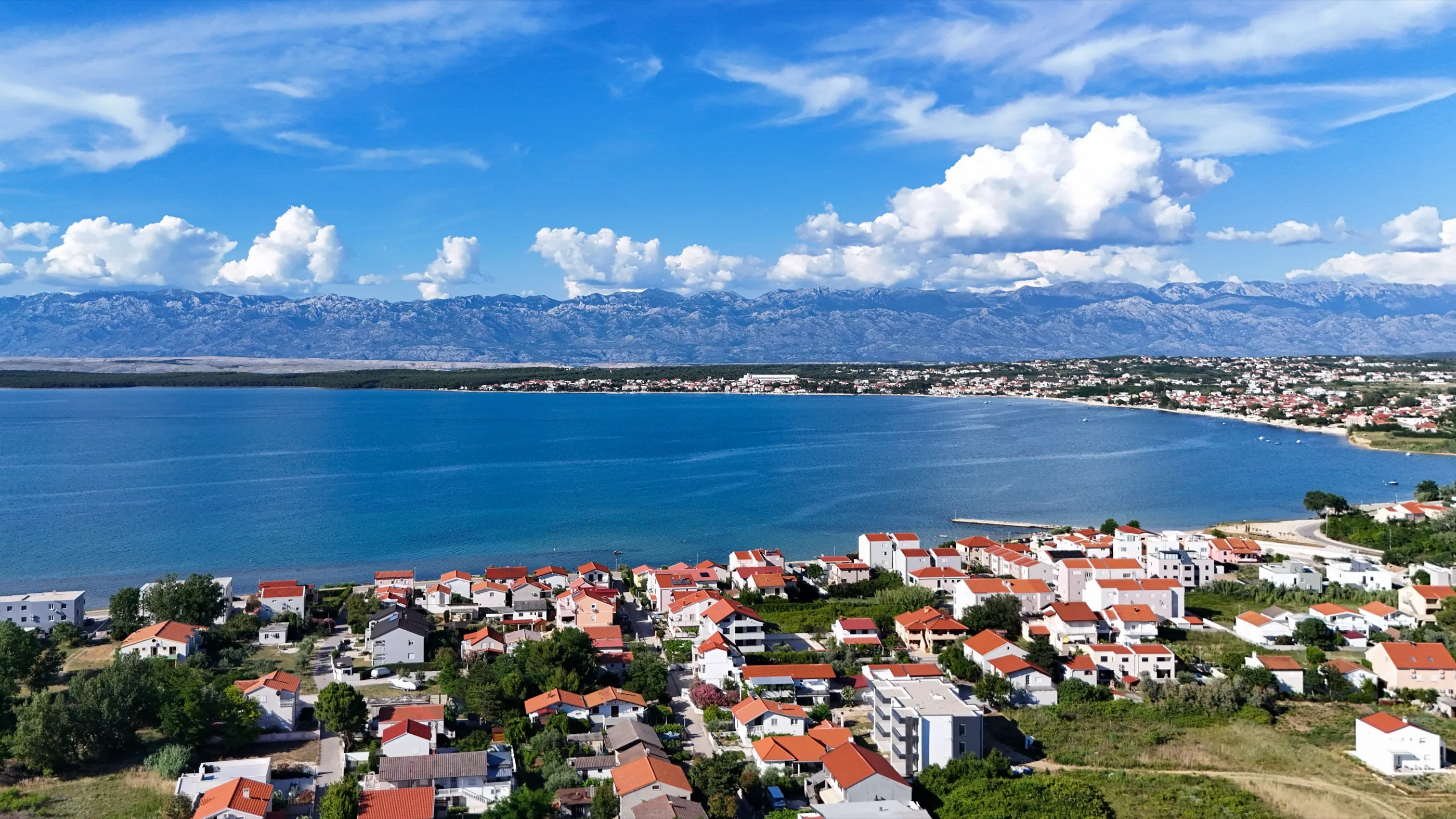 Pogled iz zraka na Ždrijac s crvenim krovovima, plavim ninskim zaljevom i Velebitom na horizontu