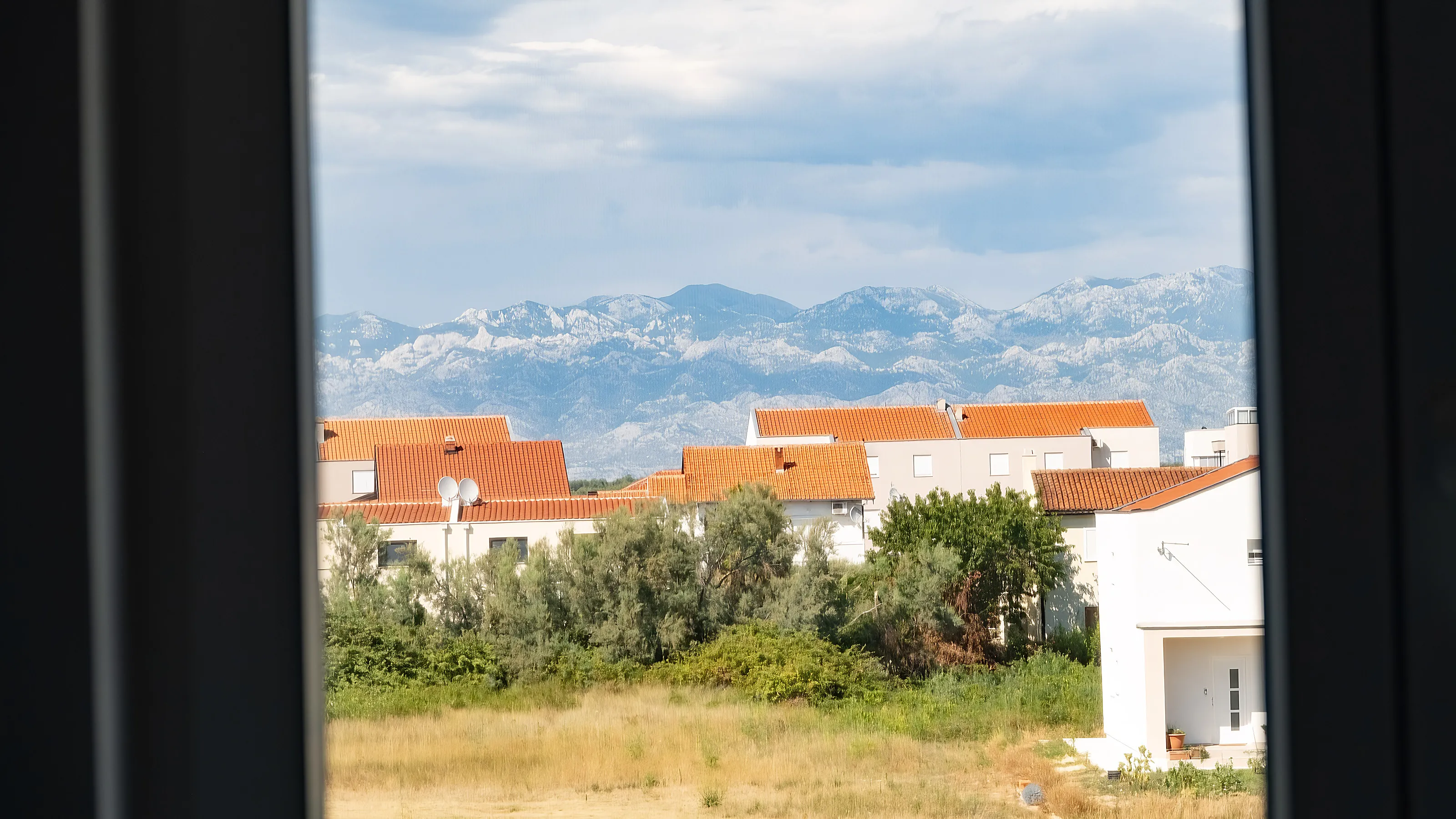 Pogled kroz prozor na crvene krovove Nina i Velebit